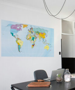 Office workspace: world map poster on wall, laptop and notebooks on a dark table with bottles and glassware nearby.