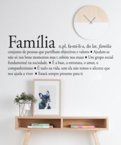 Decorative wall art in Portuguese with the word 'Familia' and a family definition, above a wooden shelf with a plant and framed art under a round clock on a white wall.