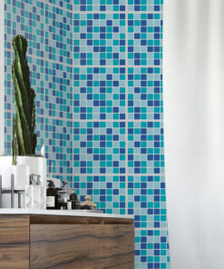 Corner of a bathroom with a blue teal mosaic tiled wall, a tall cactus in a white pot on a marble countertop, and dark wood vanity drawers below.