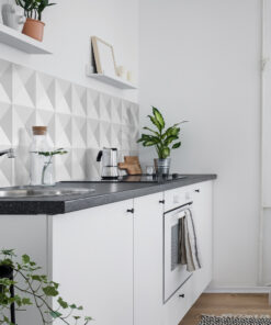 Bright white kitchen with geometric triangular tile backsplash, plants on the counter, and a stovetop with a kettle nearby.