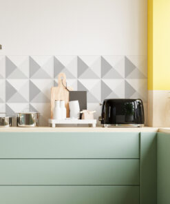 Modern kitchen counter with pastel green cabinets, geometric gray triangle backsplash, and a black toaster beside a wooden cutting board on a light wood counter.