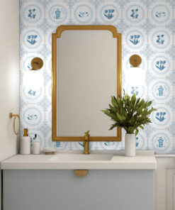 Gold-framed mirror above a white sink with blue Delft tile backsplash and a plant in a white vase on the right side of the counter.