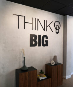 Wall art reading 'THINK BIG' with a lightbulb icon on a gray wall above dark wood cabinets displaying vases and books.