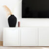 mockup final | Casadart | Vinis Autocolantes, Papel de Parede e Painéis Decorativos Black vase with tall dried pampas grass on a white cabinet beside a wall-mounted TV; a red speckled candle sits nearby.
