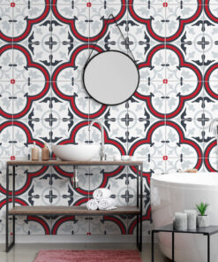 Bathroom scene with ornate geometric tile wall in red, black, and gray; vessel sink on a wooden table, chrome faucet, black metal shelving with towels, and a white bathtub nearby.