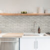 02 | Casadart | Vinis Autocolantes, Papel de Parede e Painéis Decorativos Kitchen shelf displaying glassware and white dishes over a light brick backsplash.