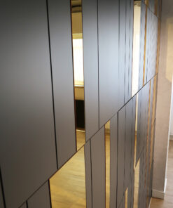 Interior view of a modern wall with tall, dark grey vertical panels and narrow gold-tinted glass strips, a wooden floor visible at the bottom.