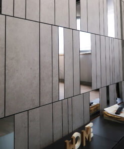 Modern interior wall of concrete panels with black grout lines and diagonal seam, plus a desk with magazines and wooden letter blocks seen on the right edge.