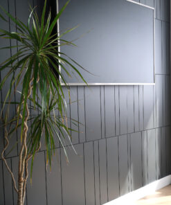 Tall indoor plant with long green leaves beside a dark gray paneled wall and light-colored floor edge