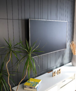 Living room with a large flat-screen TV mounted on a dark paneled wall, flanked by a tall plant and a white console with decorative wooden HOME letters nearby.