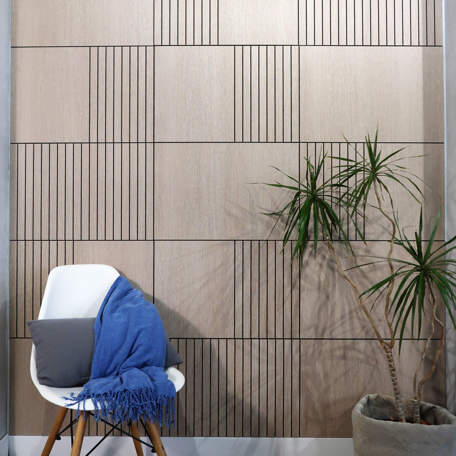 White molded chair with a blue fringed blanket, placed against a vertical wood-paneled wall; a tall plant in a pot on the right.