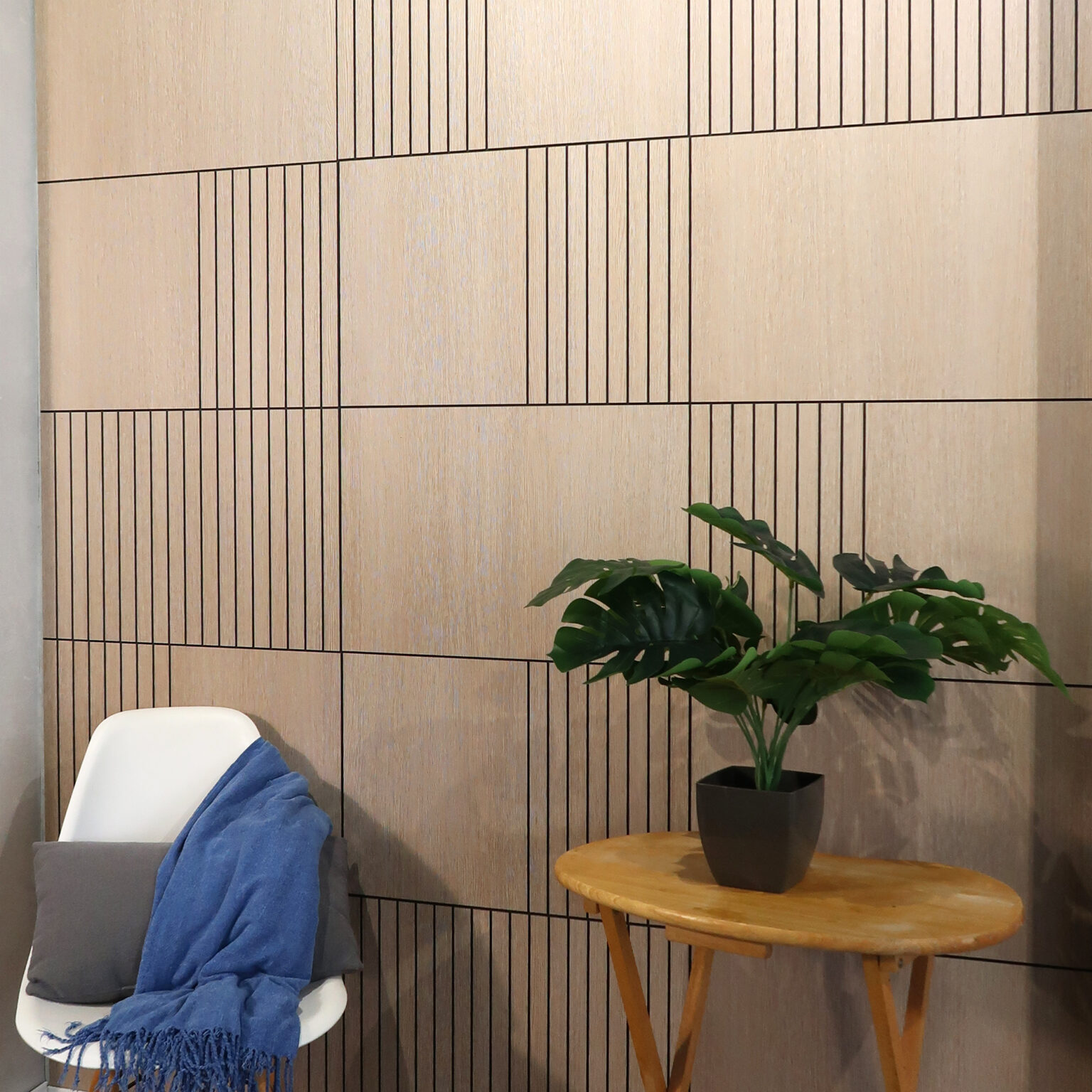 White modern chair with a blue throw draped over it, beside a small round wooden table with a potted plant against a wood-paneled wall