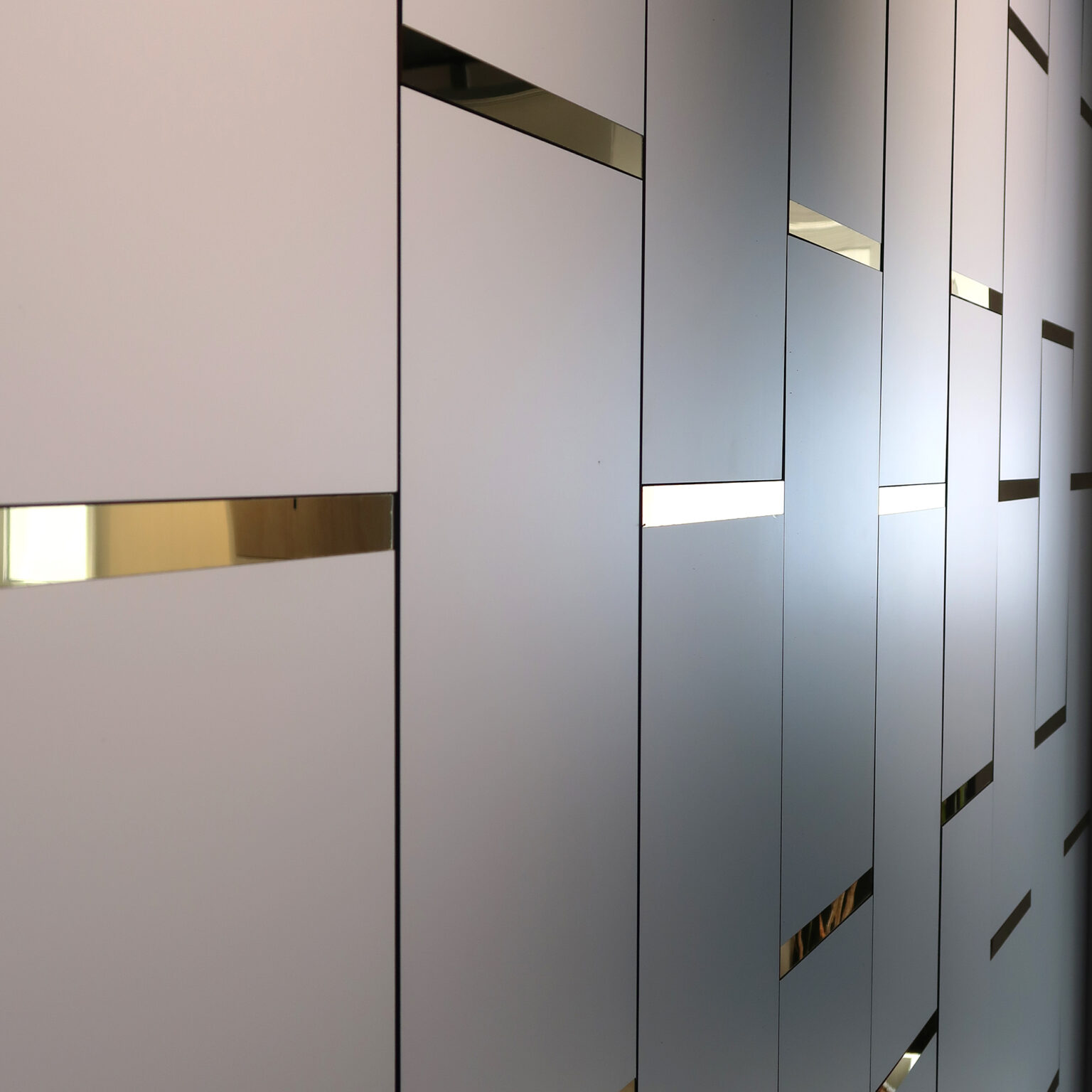 Abstract interior wall with vertical gray panels and narrow gold reflective slits creating a geometric pattern