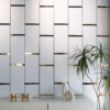| Casadart | Vinis Autocolantes, Papel de Parede e Painéis Decorativos Minimalist interior with a gray vertical-panel wall, decorative 'HOME' letters on a white counter, and a tall potted plant on the right.