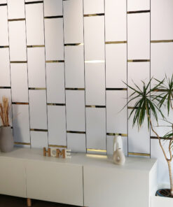 Modern white cabinet wall with gold horizontal trims, a tall plant on the right, and decorative 'HOME' letters on a white sideboard.