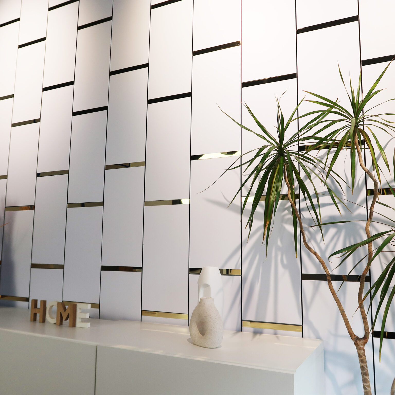 Modern interior with a white slatted wall, gold accents, and a white desk; two tall green plants appear on the right side.