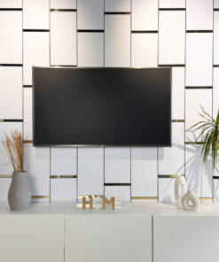 Modern living room with a wall of white panels accented by thin gold strips, a large flat-screen TV, and vases of dried grasses on a white cabinet.