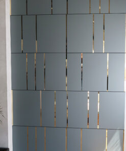 Grey vertical slatted wall with narrow gold gaps between panels; left edge shows a concrete column and a small plant in the corner