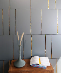 Wooden table with a tall gray vase holding dried grass and an open magazine, set against a gray slatted wall with gold gaps.