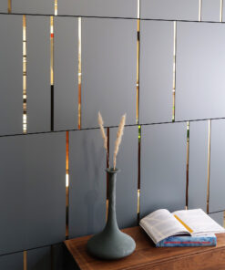 Gray slatted room divider with narrow vertical gaps exposing warm metallic reflections, a dark vase with dried grasses, and an open book on a wooden table showing 'Japanese Graphics Now!' on the spine cover.