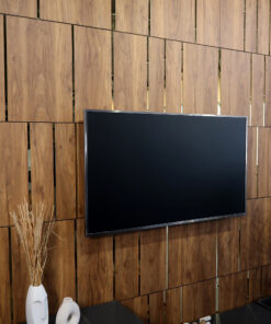 Flat-screen TV mounted on a wood-paneled wall above a black table, with decorative white vases to the left.
