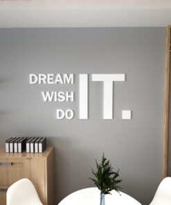 Office wall with large white letters reading 'DREAM IT WISH DO' on a gray backdrop, with a wooden cabinet and plant nearby.