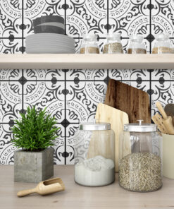 Shelf with white stacked plates and glass jars filled with grains against a black-and-white patterned tile wall, plus wooden cutting boards and a wooden spoon in the foreground.