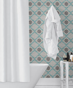 White tub in a bathroom with teal patterned tiles, a white robe hanging, and bottles on a wooden stand nearby