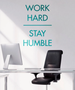 Motivational wall text reading 'Work Hard Stay Humble' above a glass desk with a silver computer and black office chair in a bright office setting.