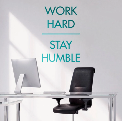 CapturarPNG1 | Casadart | Vinis Autocolantes, Papel de Parede e Painéis Decorativos Motivational wall text reading 'Work Hard Stay Humble' above a glass desk with a silver computer and black office chair in a bright office setting.