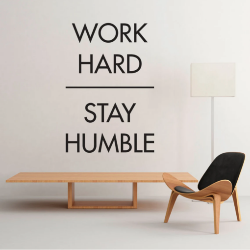 | Casadart | Vinis Autocolantes, Papel de Parede e Painéis Decorativos Minimalist room with a large wall quote: 'Work hard Stay humble', plus a wooden bench and a modern chair.