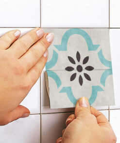 Hands smoothing a decorative tile sticker onto a white tiled wall.
