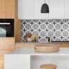 | Casadart | Vinis Autocolantes, Papel de Parede e Painéis Decorativos Modern kitchen with light wood cabinets, a white island, and a black-and-white patterned tile backsplash, plus a woven basket on the counter.
