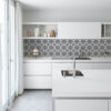 | Casadart | Vinis Autocolantes, Papel de Parede e Painéis Decorativos Bright white kitchen with a central island sink, chrome faucet, and a black-and-white geometric tile backsplash.