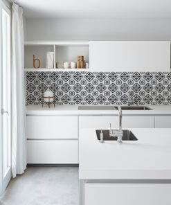 Bright white kitchen with a central island sink, chrome faucet, and a black-and-white geometric tile backsplash.