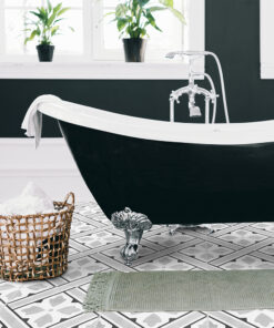 Black clawfoot bathtub with a white rim in a bright bathroom, tiled geometric floor, and a wicker basket of bath salts nearby.