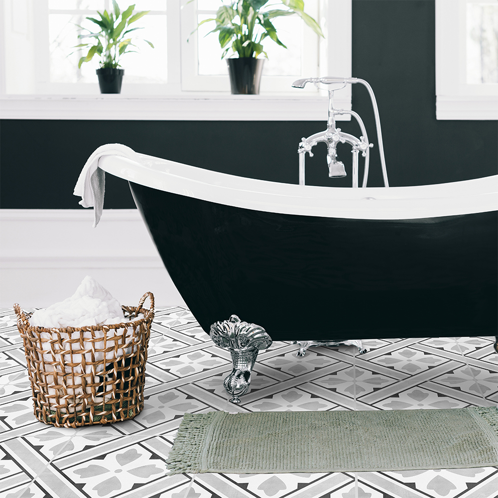 01 | Casadart | Vinis Autocolantes, Papel de Parede e Painéis Decorativos Black clawfoot bathtub with a white rim in a bright bathroom, tiled geometric floor, and a wicker basket of bath salts nearby.