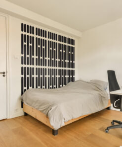 Bedroom with a low wooden bed frame and gray bedding, beside a white wall featuring a tall black vertical panel pattern behind the bed.