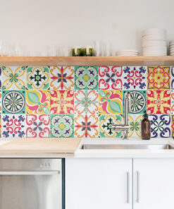Colorful tiled backsplash above a white countertop with a stainless steel sink and faucet in a bright kitchen.