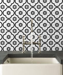 Chrome kitchen faucet over a white sink on a dark counter, with a bold black-and-white floral tile backsplash in the background.