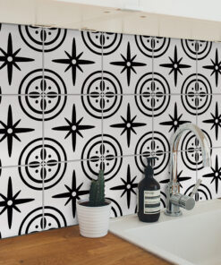 Kitchen backsplash with bold black circular and starburst tiles behind a white sink, with a small potted cactus and a soap dispenser on the wooden counter.