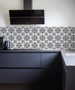 Modern black-kitchen scene with patterned tile backsplash, upper range hood, and dark cabinetry surrounding a sleek countertop.