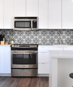 Modern kitchen with stainless steel stove and microwave, white cabinets, and a black-and-white patterned tile backsplash.