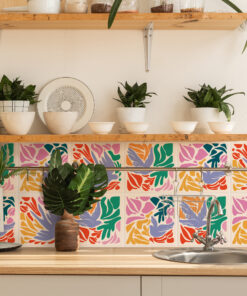 Wooden shelf with white bowls and glass jars, flanked by green potted plants above a wooden counter in a bright kitchen.
