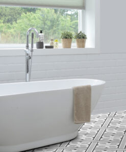 Bright bathroom featuring a white freestanding tub with a beige towel, chrome faucet, and a windowsill with small potted plants and toiletries; patterned floor tiles.