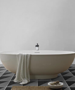 White freestanding bathtub in a bathroom with a striped towel draped over the side and black-and-white geometric tile flooring out front.