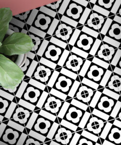 Potted plant with large green leaves rests on a diagonal black-and-white geometric tile floor, with a pink surface visible above.