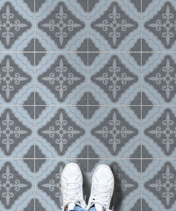 Top-down view of white sneakers standing on blue-gray patterned ceramic tiles with an ornate repeating motif.