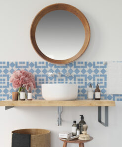 Round wooden-framed mirror above a white vessel sink, with a blue geometric tile backsplash and pink peonies on the counter edge.