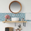 | Casadart | Vinis Autocolantes, Papel de Parede e Painéis Decorativos Round wooden-framed mirror above a white sink with a blue geometric tile backsplash, pink flowers, and bathroom products on a wooden shelf and wicker basket nearby.
